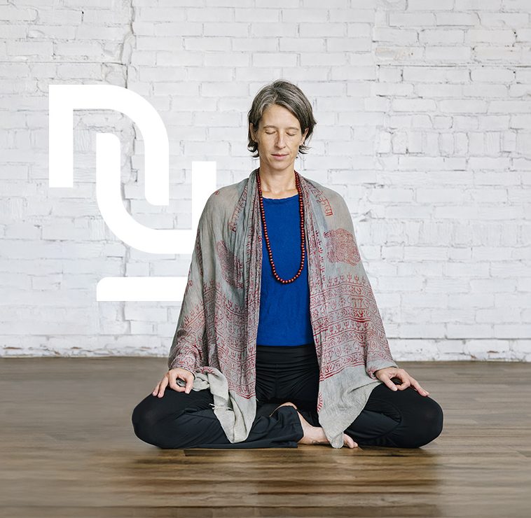 Personnes assise en posture de méditation, les yeux fermés, dans un studio lumineux au mur de briques blanches.